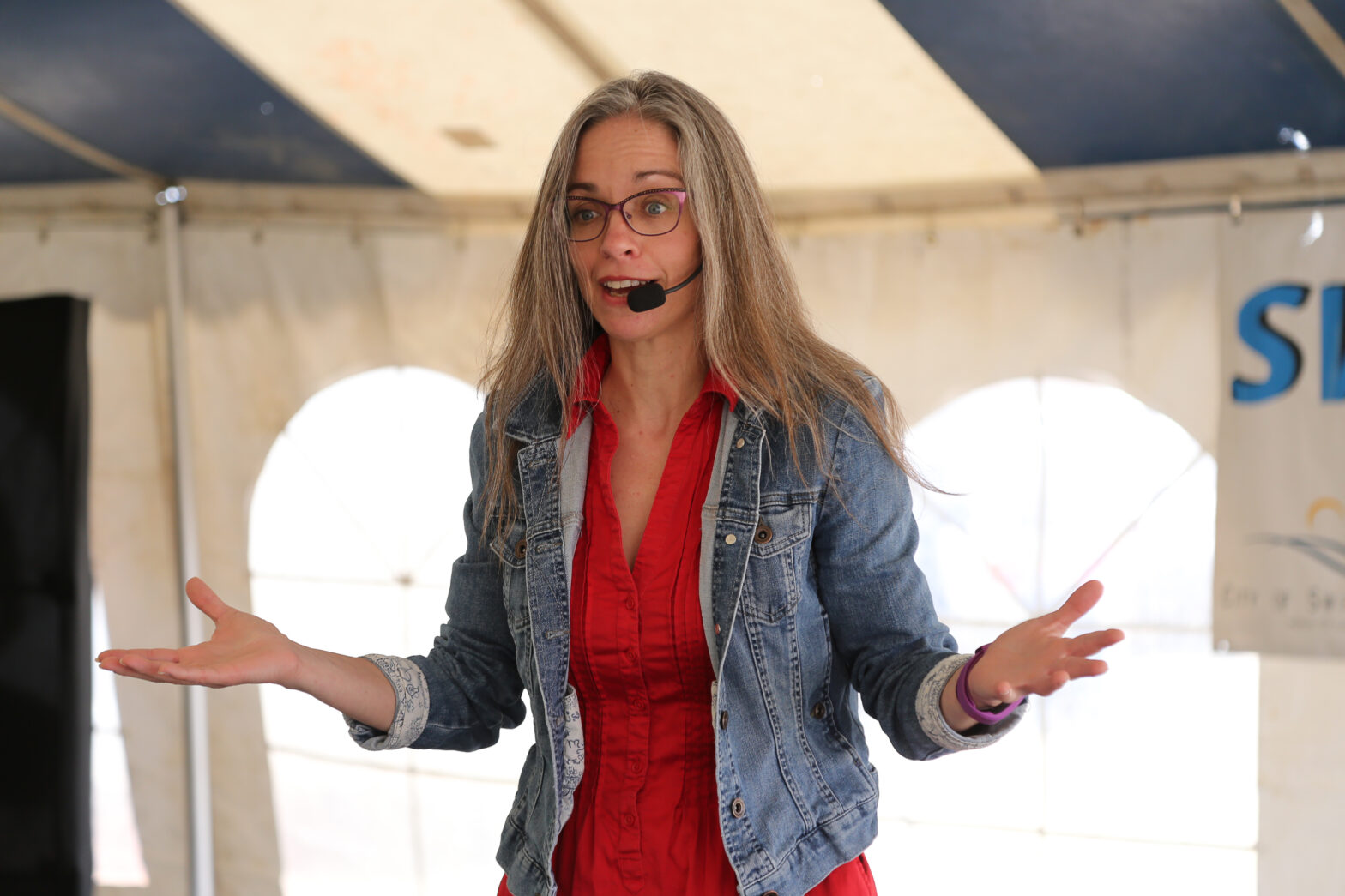 woman in a red dress and blue denim jacket wearing a headset microphone and telling stories